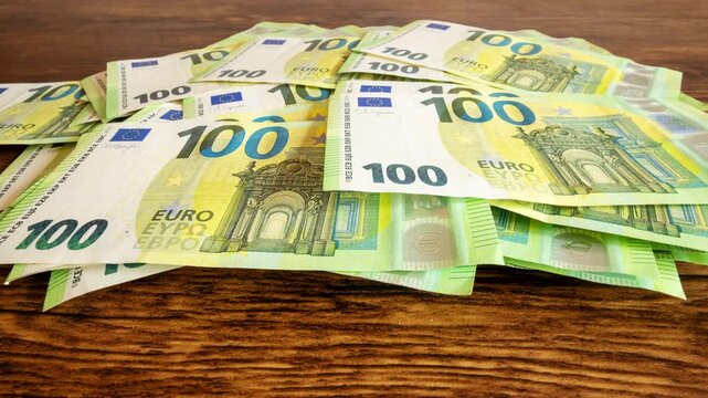 Pile of one hundred euro banknotes on wooden table. Cash background representing wealth, success and financial profit, 4k