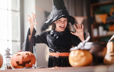 Obraz premium Joyful Girl in Witch Costume Celebrating Halloween with Pumpkins