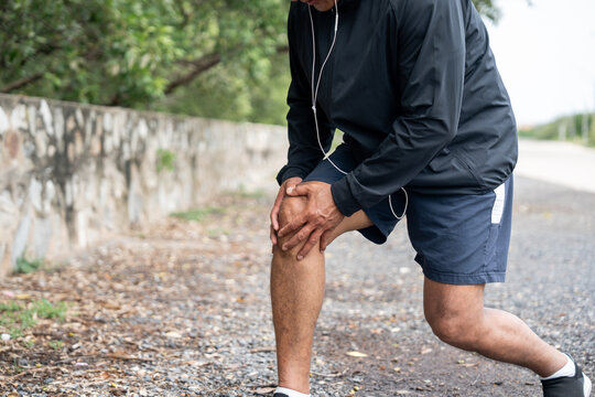 Mature man tired and leg pain during jogging at nature park. Runner has sore knees because he has been running for too long. Exercising until the injury. Training athlete work out at outdoor.
