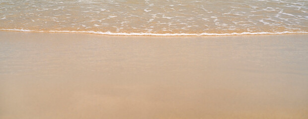 Obraz premium Clean sandy beach by the ocean, small waves with foam washing the shore, close-up view of golden yellow sand from copy space.