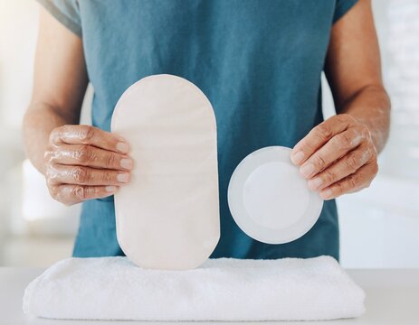 Hands holding a plain ostomy pouch and skin barrier flange to prepare stoma care supplies at home