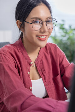 Woman eyeglass smile portrait shirt indoor office Asian casual laptop happy woman wearing eyeglass and red shirt working indoors with relaxed expression in bright modern workspace Vertical