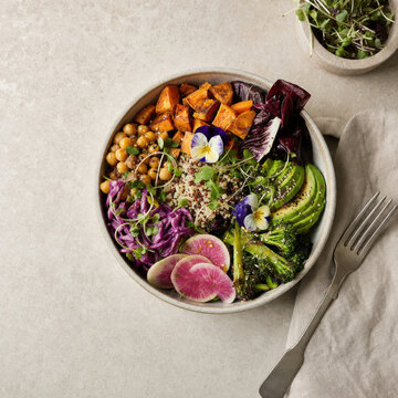 Healthy bowl of vegetables and grains served in a dish on a light surface with a fork and a cloth