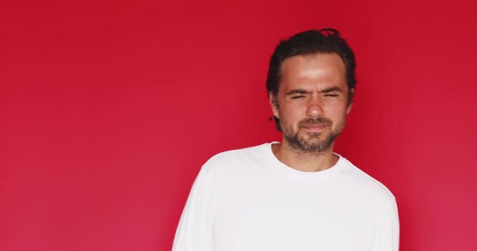 Middle aged Caucasian man knocking on invisible door, wincing with closed eyes and uncomfortable expression in fear of bad news on vivid red studio background, hesitation cringe video
