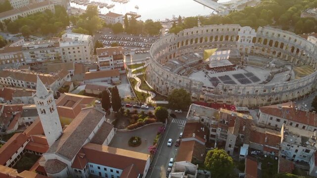 Aerial drone view of the ancient Roman amphitheater overlooking the Adriatic Sea at golden hour in Pula, Croatia.