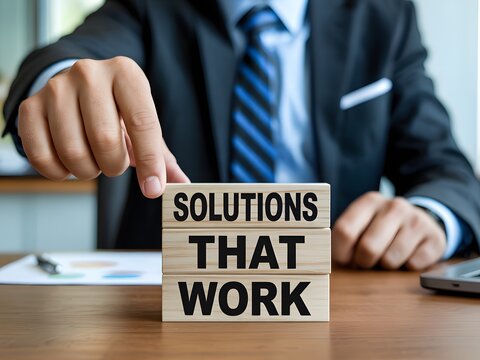 Businessman placing wooden blocks spelling Solutions That Work on a professional office desktop