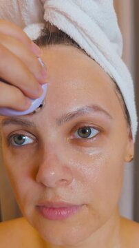 Woman performing a microcurrent facial treatment at home, applying a skincare device to her forehead to tighten skin and improve elasticity, promoting a refreshed and youthful complexion