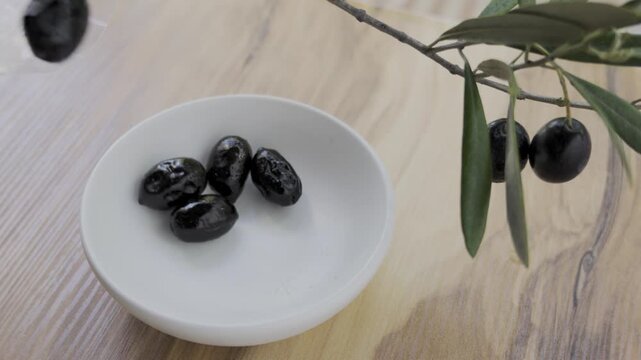 Dropping ripe black olives into white bowl wooden table 4k