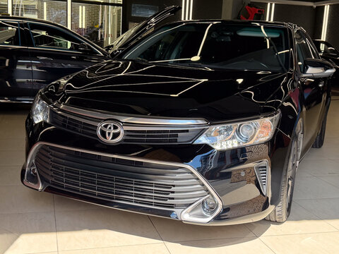 Front view of black Toyota Camry XV50 Japanese sedan car inside professional auto detailing workshop garage box with modern led lighting lamps, luxury executive business automobile, tuning industry.