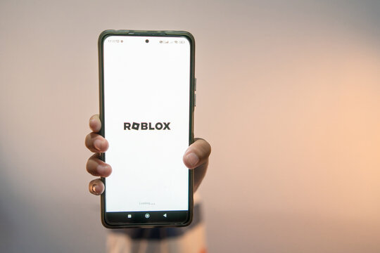 Riau, July 26, 2026, Hand holding a smartphone displaying the Roblox app loading screen against a soft neutral background. Perfect for gaming, technology, and mobile app concepts.
