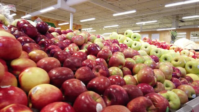 Handheld shot of a variety of apples piled for display in the produce section of a grocery store market.