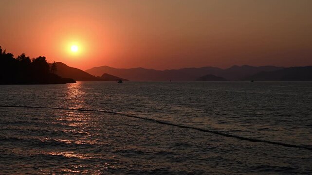 A timelapse of a shining golden sunset over the Mediterranean Sea with silhouettes of mountains on the horizon. Summer in Fethiye, Turkey

