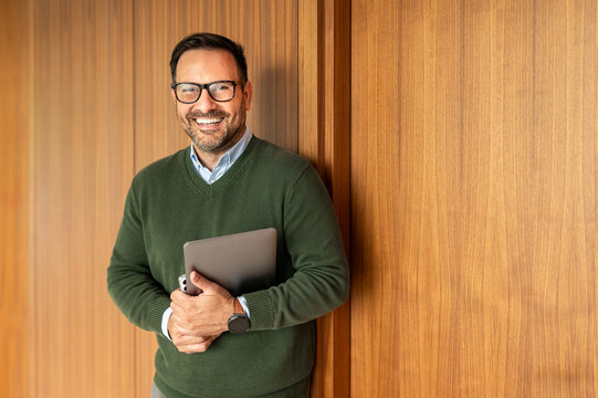Businessman in eyeglasses holding a digital tablet, smiling and looking confident, embodying professionalism, leadership, and success in a modern office environment