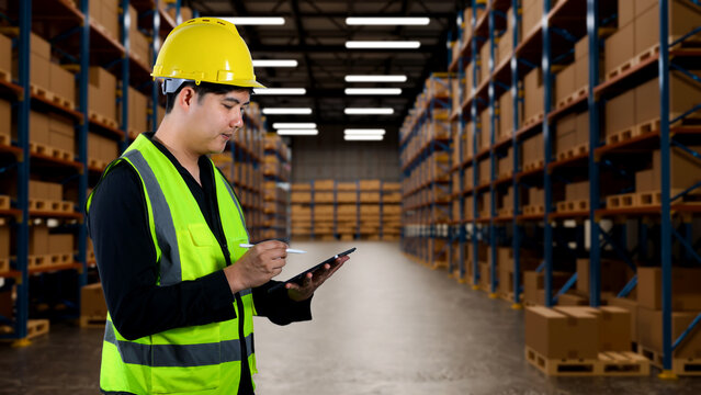 Warehouse Worker in Safety Vest and Yellow Hardhat Using Digital Tablet for Inventory Management in Large Storage Facility