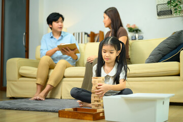 Fototapeta premium Asian Girl Playing Jenga Wood Blocks While Parents Consult with Professional at Home