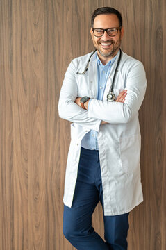 Smiling male physician standing with arms crossed, wearing a lab coat and stethoscope, portraying medical authority, trust, health services, and professional competence