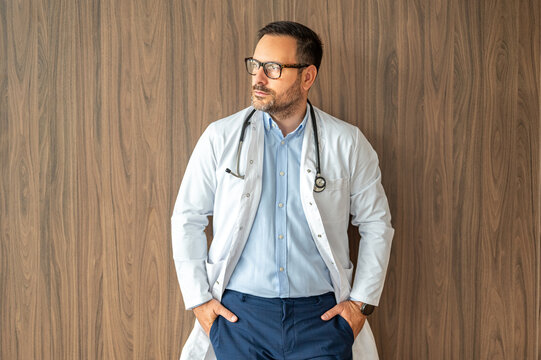 Confident medical practitioner wearing eyeglasses and lab coat, looking away, reflecting on healthcare challenges and professional dedication while standing against a textured backdrop