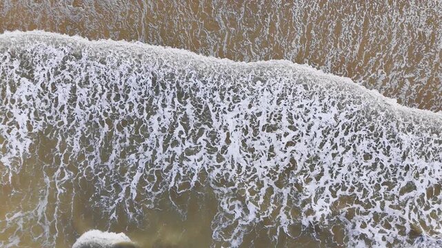 Foam pattern from incoming wave on wet sand, top down drone view. Natural seaside texture and abstract background