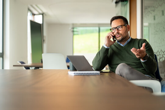 Entrepreneur managing business communication with a client, talking on a mobile device while working remotely, discussing project details during a video conference