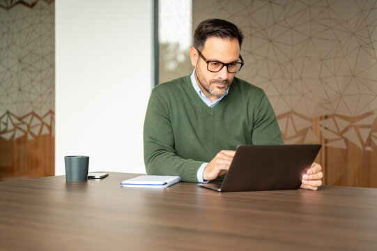 Professional man using a laptop computer at a conference table, focusing on online work, remote business, and digital communication in a modern office environment