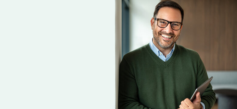Smiling mature businessman holding a digital tablet in modern office, portraying confidence and successful entrepreneurship in a professional workplace setting