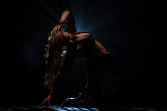 Attractive female dancer posing on floor under bright blue spotlight. Concept of expressive artistic layout for music album cover, theater poster and modern dancing class promotion.