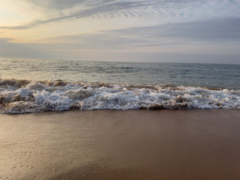  A spilling wave bursts into sea foam on a sandy shore, glowing in warm golden evening light. Textured water and shimmering reflections capture the moment where the ocean meets the beach.
