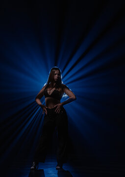 Expressive female dancer posing on dark stage illuminated by deep blue light rays. Concept of commercial artwork template for music album cover, theater flyer and creative show promotion.