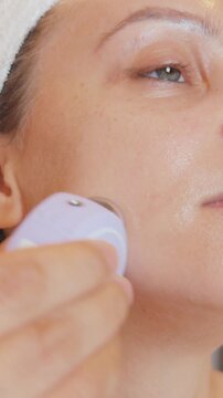 Woman applying a microcurrent device along her cheek, performing an advanced anti aging skincare procedure that stimulates facial muscles for improved skin elasticity and a youthful appearance