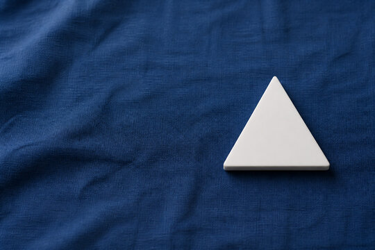 Single white equilateral triangle object on deep blue linen, calm still life for editorial concept