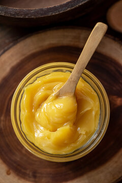 Ghee butter in glass jar with wooden spoon on wooden table with blurred background.