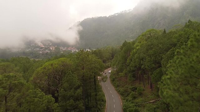 An Aerial shot of a car moving on the Roosi by pass road near Nainital Surrounded with pine trees on both sides 