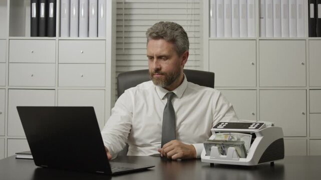 Businessman working on laptop with stacks of money in office. Business concept with cash and digital work. Banker in office. Finance management concept with money. Businessman accountant in office.