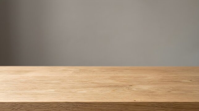 A close up view of an empty wooden table surface with a blurred grey wall background for product display purposes