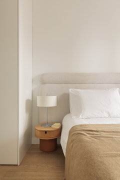 Round oak bedside table with slender cylindrical lamp