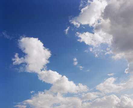 Airplane Crossing Blue Sky Between Dramatic White Clouds