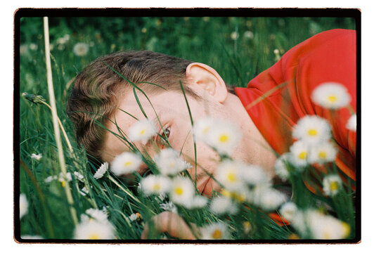 A man lies still among daisies in long summer grass