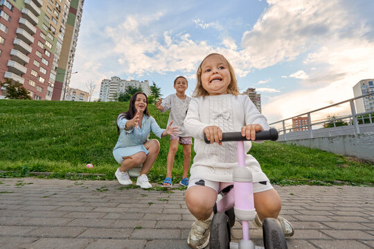 Toddler Riding Balance Bike With Funny Expression While Family Support