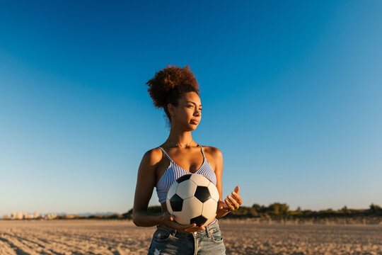 Young woman holding soccer ball on beach at sunset