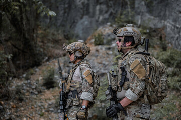 Fototapeta premium Two armed military operators secure an area during a tactical mission, holding rifles while patrolling a dense forest wilderness for defensive strategy, combat readiness, and national security.