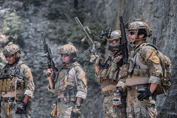 Fototapeta premium Professional tactical team standing in defensive line against rugged mountain cliff. Elite soldiers in combat gear maintaining high alert during field operation, military training or security mission.