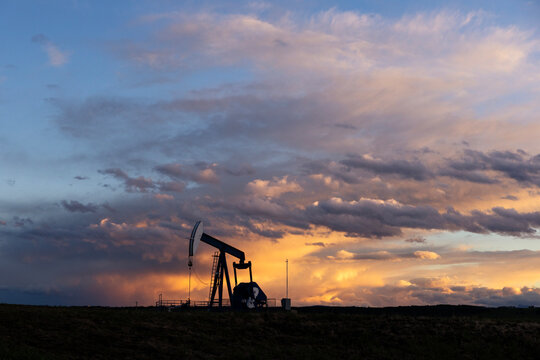 Oil Pump Jack Works at Sunset Under Clouds in the Field
