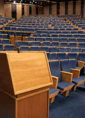 Fototapeta premium Wooden podium with microphone stands in front of rows of blue upholstered seats in an empty auditorium. The space conveys readiness for a lecture or presentation.