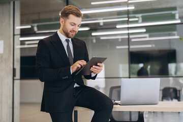 Fototapeta premium Businessman using tablet, focused on work tasks in a contemporary office setting with a laptop nearby