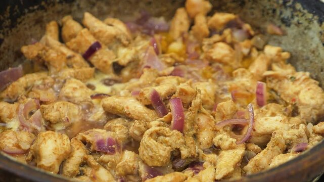 Chicken marinated in teriyaki sauce and spices is fried in a deep cast-iron skillet in vegetable oil and stirred with a spatula. Medium shot.