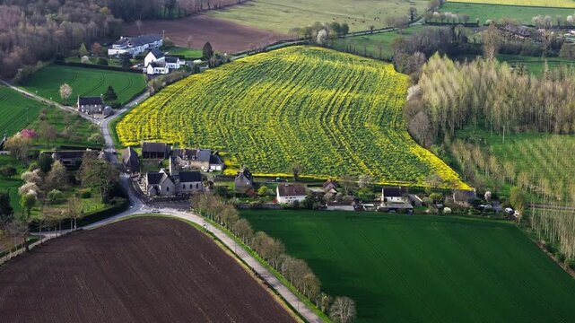 Aerial view of small rural village in Normandy, France, surrounded by green farmland, country roads and spring fields. Traditional French countryside landscape