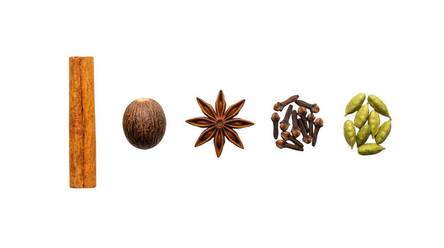 Cinnamon stick nutmeg star anise cloves and cardamom pods arranged in a row