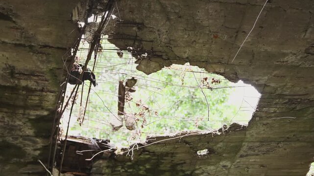 Decaying concrete roof with large irregular hole revealing sky and foliage through damaged structure