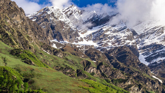 Himachal Pradesh snow capped Himalayan mountain peaks rising above green grassy valley slopes under blue sky