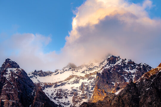 Snow-Covered Himalayan Mountain Peaks Rising Above Dramatic Clouds Under a Clear Blue Sky